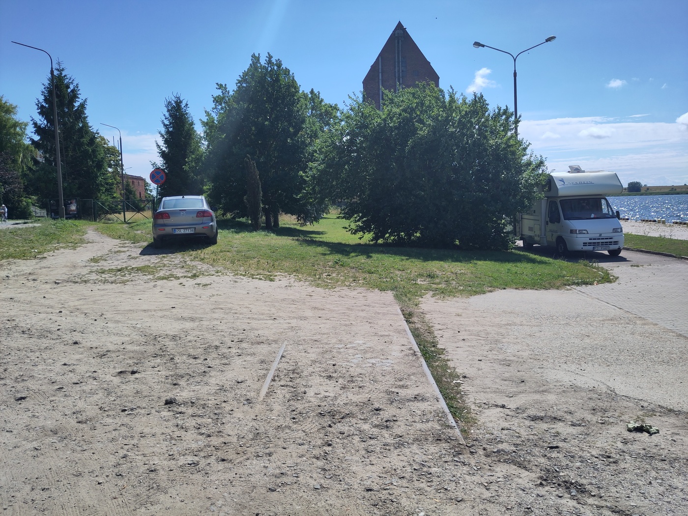 Krótki odcinek szyn zakopanych w piasku, w tle wysoki ceglany budynek
